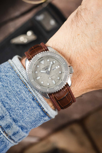 Seiko 5 Sports dive watch on a brown alligator-grain leather strap, shown on wrist with a silver dial and matching silver bezel.