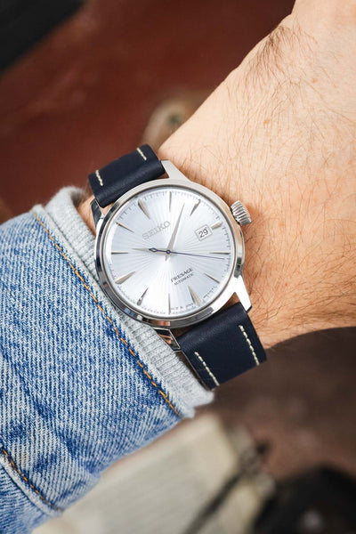 Seiko Presage automatic watch on a navy blue leather strap with cream contrast stitching, shown on wrist with a silver sunburst dial and stainless steel case.