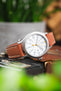 Timex Expedition-style field watch on a tan leather strap with cream contrast stitching, displayed on vintage camera equipment with a white dial and brushed grey case.