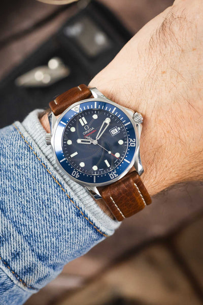 Omega Seamaster Diver 300M watch on a brown leather strap with cream contrast stitching, shown on wrist with a blue dial and matching blue bezel.