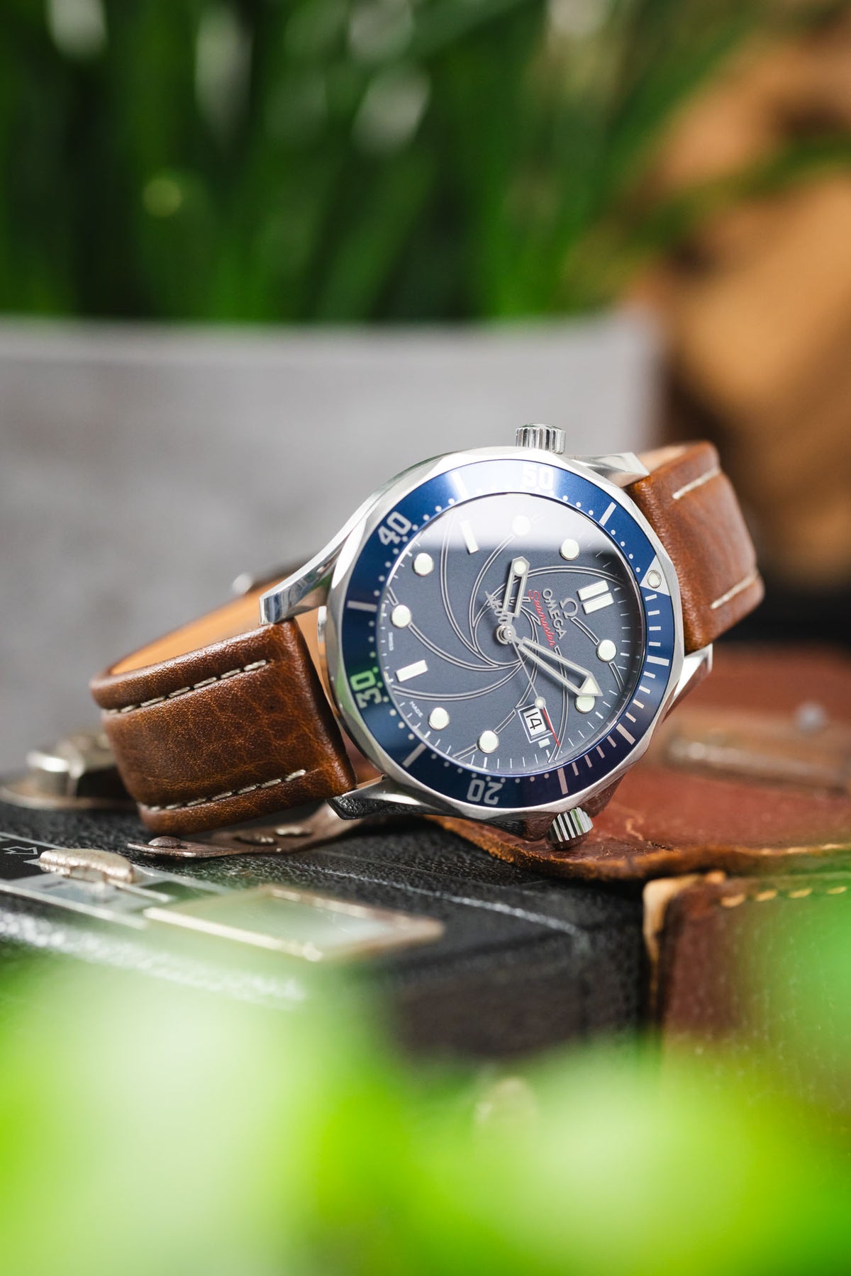 Omega Seamaster Diver 300M watch on a brown leather strap with cream contrast stitching, displayed on vintage camera equipment with a blue dial and matching blue bezel.