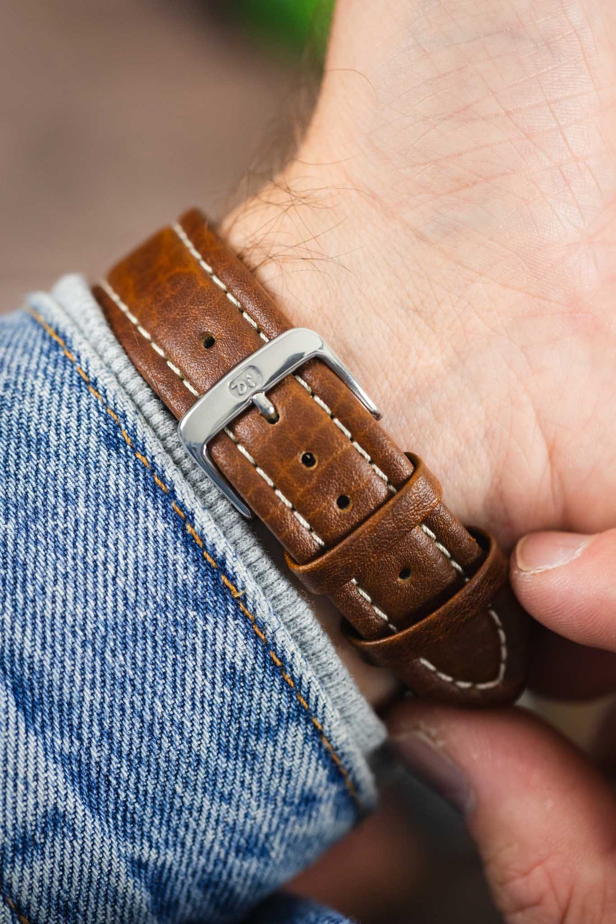 Brown vintage-style leather watch strap with cream contrast stitching and a polished stainless steel buckle, shown on wrist from the underside.