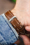 Brown vintage-style leather watch strap with cream contrast stitching and a polished stainless steel buckle, shown on wrist from the underside.
