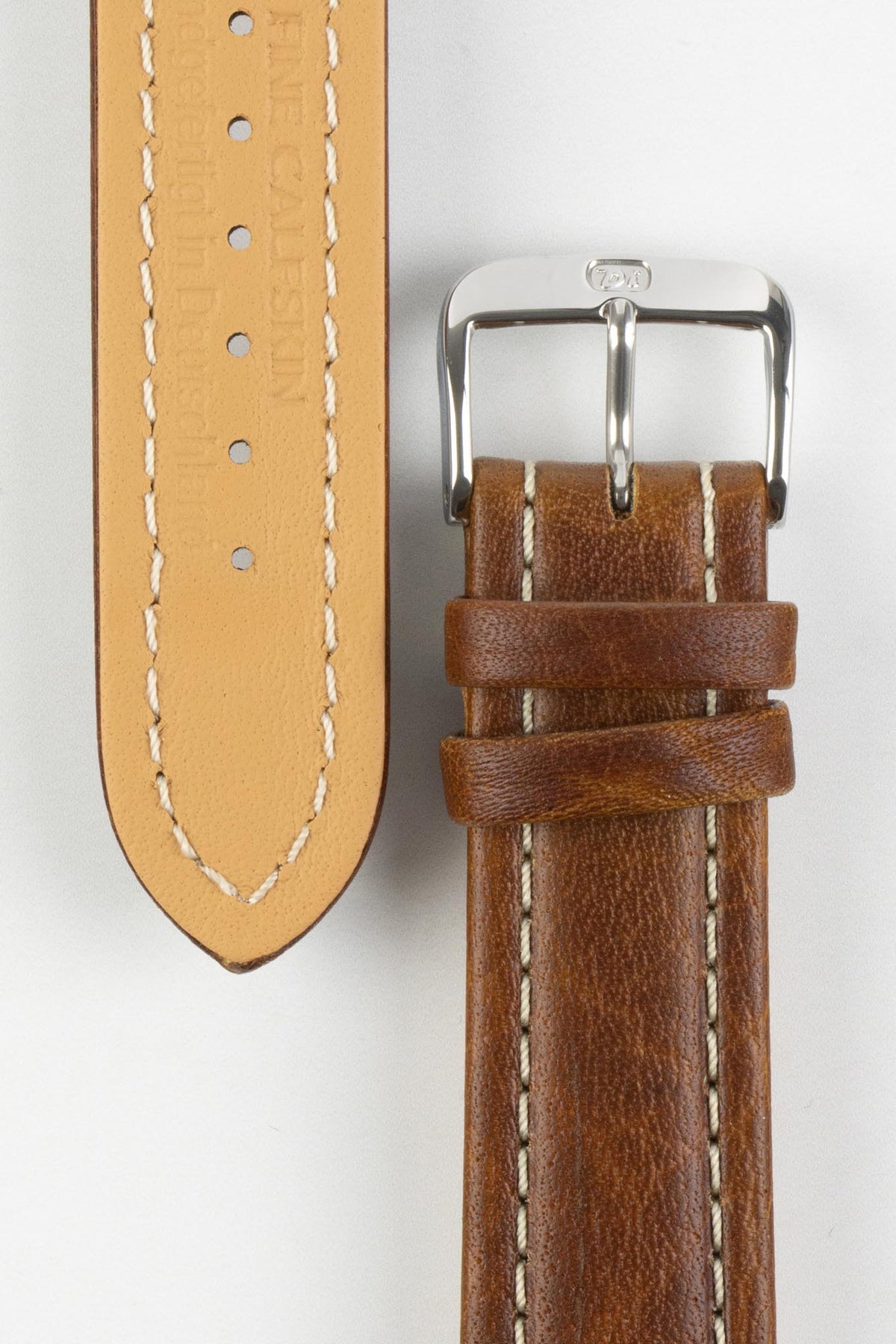 Close-up product photograph of a brown vintage-style leather rally watch strap displayed on a white background. The image shows both the top and underside of the strap, highlighting the smooth distressed leather finish, contrasting cream stitching, beige leather lining, matching brown leather keepers, and a polished stainless steel pin buckle engraved with the manufacturer's logo. The photograph showcases the strap's premium craftsmanship, padded construction, and classic motorsport-inspired design.