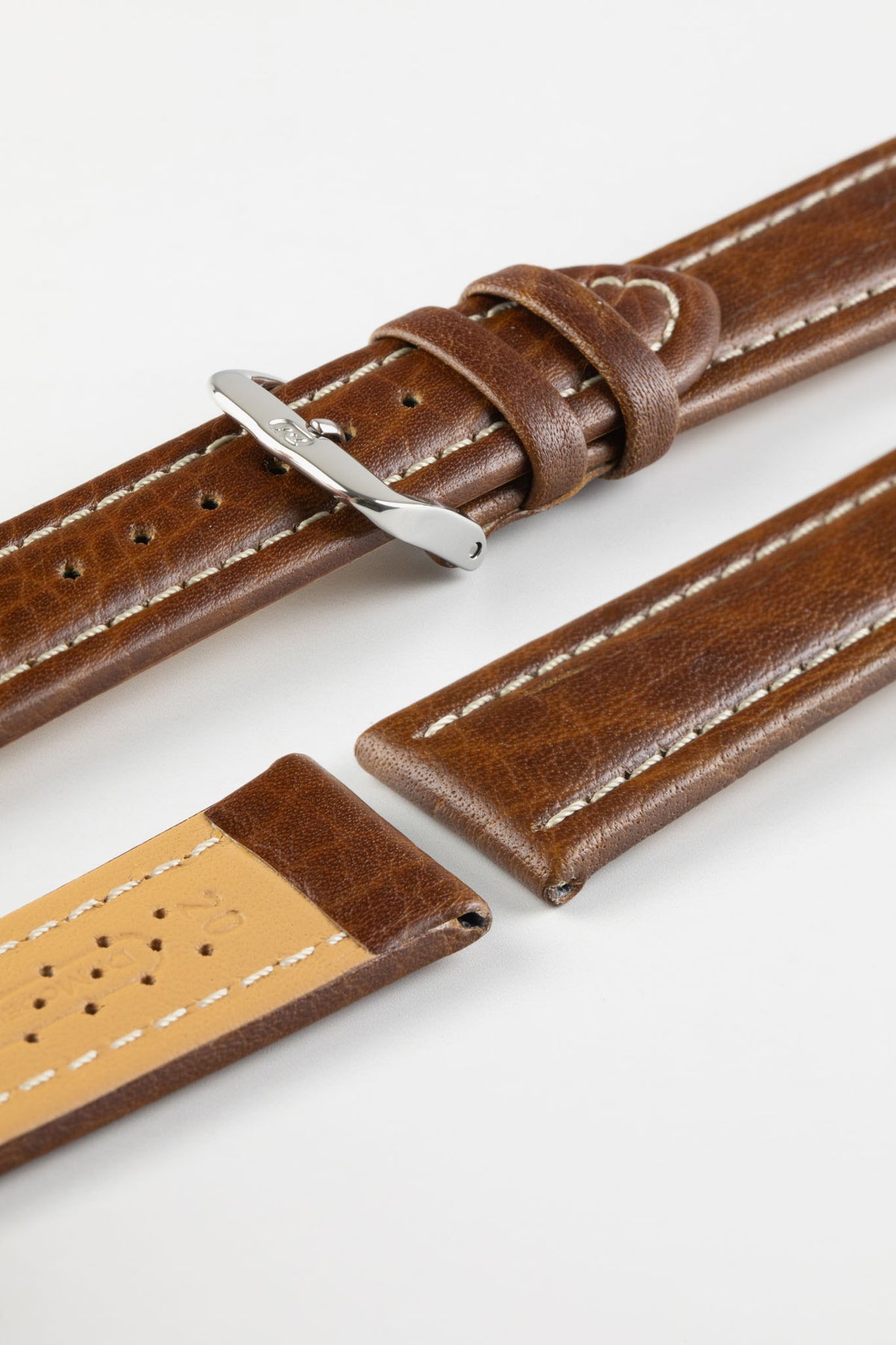 Close-up product photograph of a brown vintage-style leather rally watch strap displayed on a white background. The strap is shown in multiple sections, highlighting the smooth distressed leather finish, contrasting cream stitching, polished stainless steel pin buckle, and beige perforated leather lining. The padded construction and elongated perforated rally channels showcase the strap's motorsport-inspired design, premium craftsmanship, and comfortable wear.