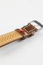 Close-up product photograph of a brown vintage-style leather rally watch strap displayed on a white background. The image highlights the underside of the strap, featuring a beige leather lining with perforated holes, contrasting cream stitching, brown leather keepers, a polished stainless steel pin buckle, and a red branded fabric tab. The distressed leather finish showcases the strap’s handcrafted character, breathable design, and motorsport-inspired styling.