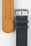 Close-up detail view of a dark navy nubuck leather watch strap, showcasing a soft suede-like texture, tonal stitching, dual keeper loops, and a polished stainless steel buckle, displayed alongside the natural tan leather lining embossed with “Handgefertigt in Deutschland” on a light grey background to highlight the premium handcrafted construction and contrasting underside.