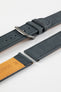 Close-up detail view of a dark navy nubuck leather watch strap featuring a soft matte finish, tonal stitching, dual keeper loops, multiple adjustment holes, a brushed stainless steel buckle, and a natural tan leather lining stamped with size markings, displayed with one strap section detached on a light grey background to highlight the supple suede-like texture, contrasting underside, and premium handcrafted construction.