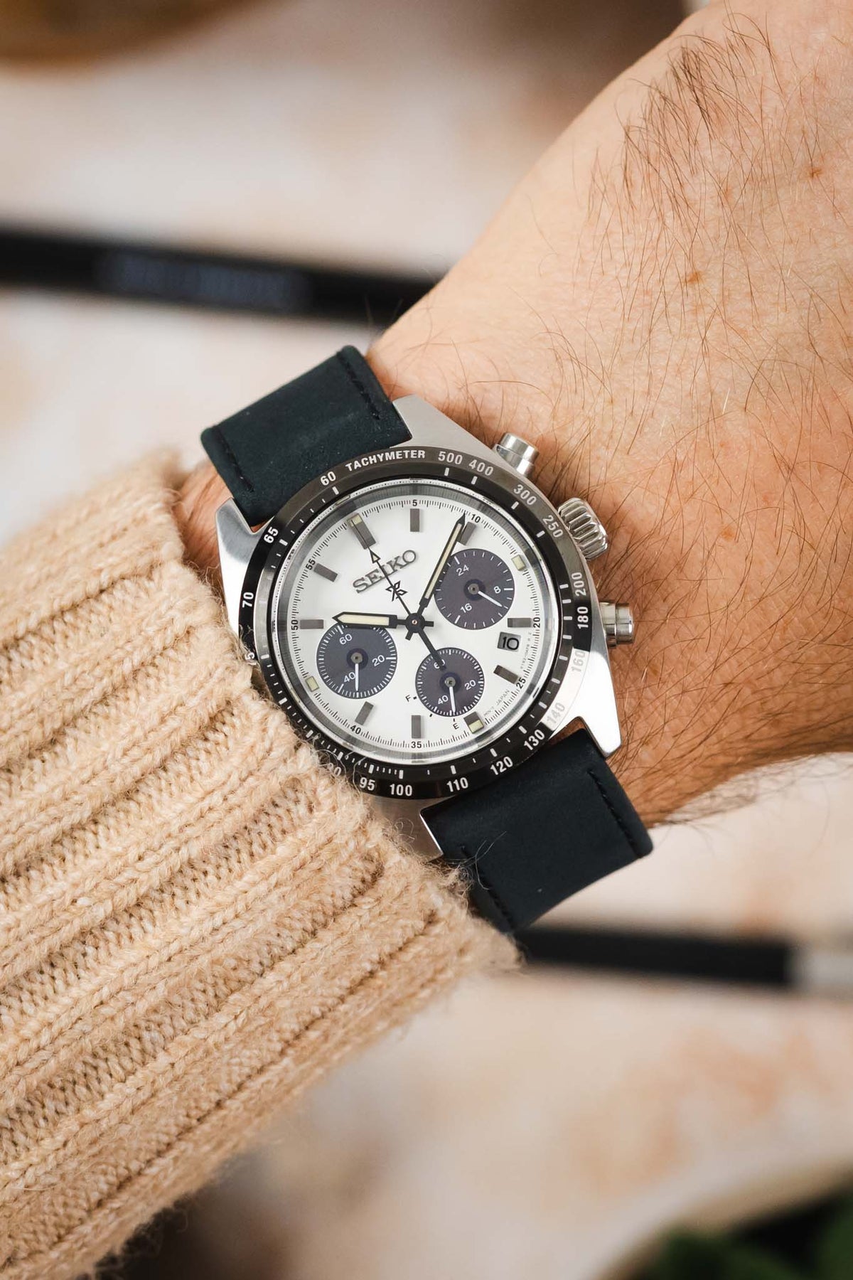 Seiko Speedtimer chronograph watch worn on the wrist, featuring a white panda dial with three dark blue chronograph sub-dials, black tachymeter bezel, stainless steel case, and a dark navy leather watch strap with tonal stitching, paired with a cream knitted sweater cuff to highlight the strap's smooth matte finish, minimalist design, and versatile everyday style.