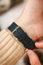 Close-up of a dark navy leather watch strap worn on the wrist, featuring a smooth matte finish, tonal black stitching, dual keeper loops, multiple adjustment holes, and a brushed stainless steel buckle, shown with a cream knitted sweater cuff to highlight the strap's minimalist design, supple leather construction, and comfortable everyday fit.
