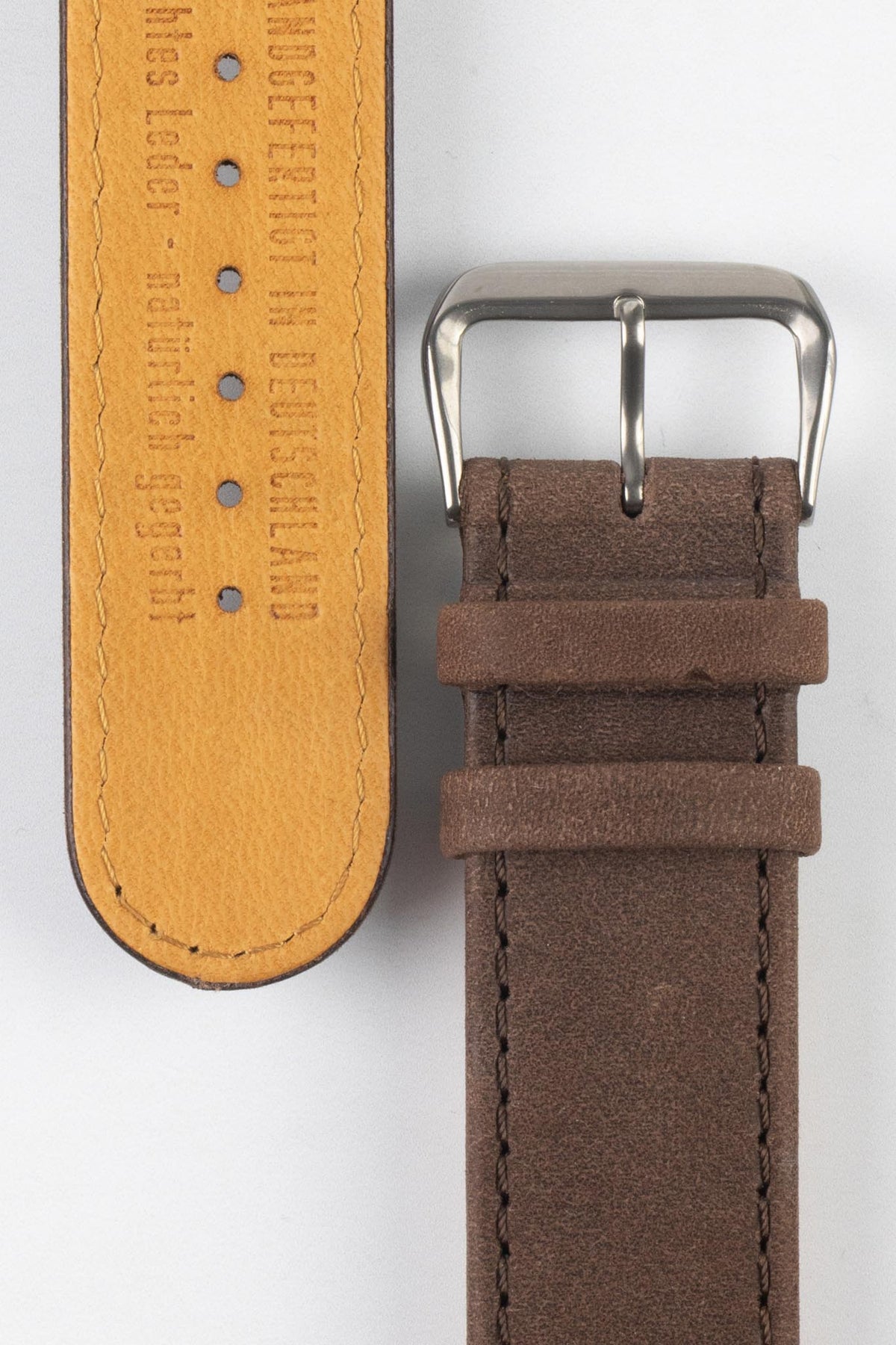 Front and back detail view of a brown nubuck leather watch strap featuring a soft matte finish, tonal brown stitching, dual keeper loops, a polished stainless steel buckle, and a natural tan leather lining embossed with “Handcrafted in Deutschland,” displayed on a light grey background to highlight the premium leather construction, contrasting underside, and vintage-inspired design.