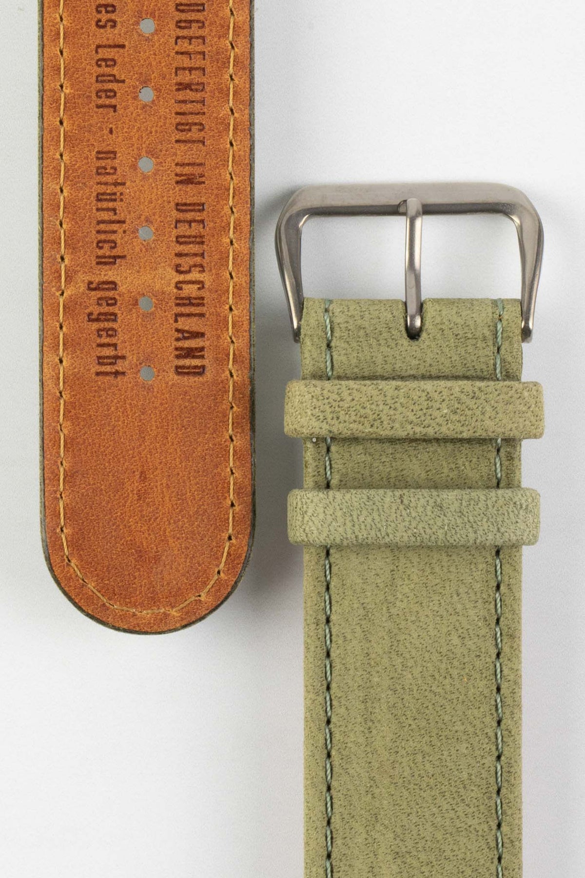 Front and back detail view of a sage green nubuck leather watch strap featuring a soft matte finish, tonal green stitching, dual keeper loops, a polished stainless steel buckle, and a natural tan leather lining embossed with “Handgefertigt in Deutschland”, displayed on a light grey background to highlight the premium handcrafted construction, contrasting underside, and vintage-inspired suede texture.