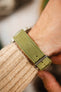 Close-up of a sage green nubuck leather watch strap worn on the wrist, featuring tonal green stitching, a soft suede-like texture, multiple adjustment holes, and a brushed stainless steel buckle, shown with a cream knitted sweater cuff to highlight the strap's premium handcrafted construction, comfortable fit, and vintage-inspired character.