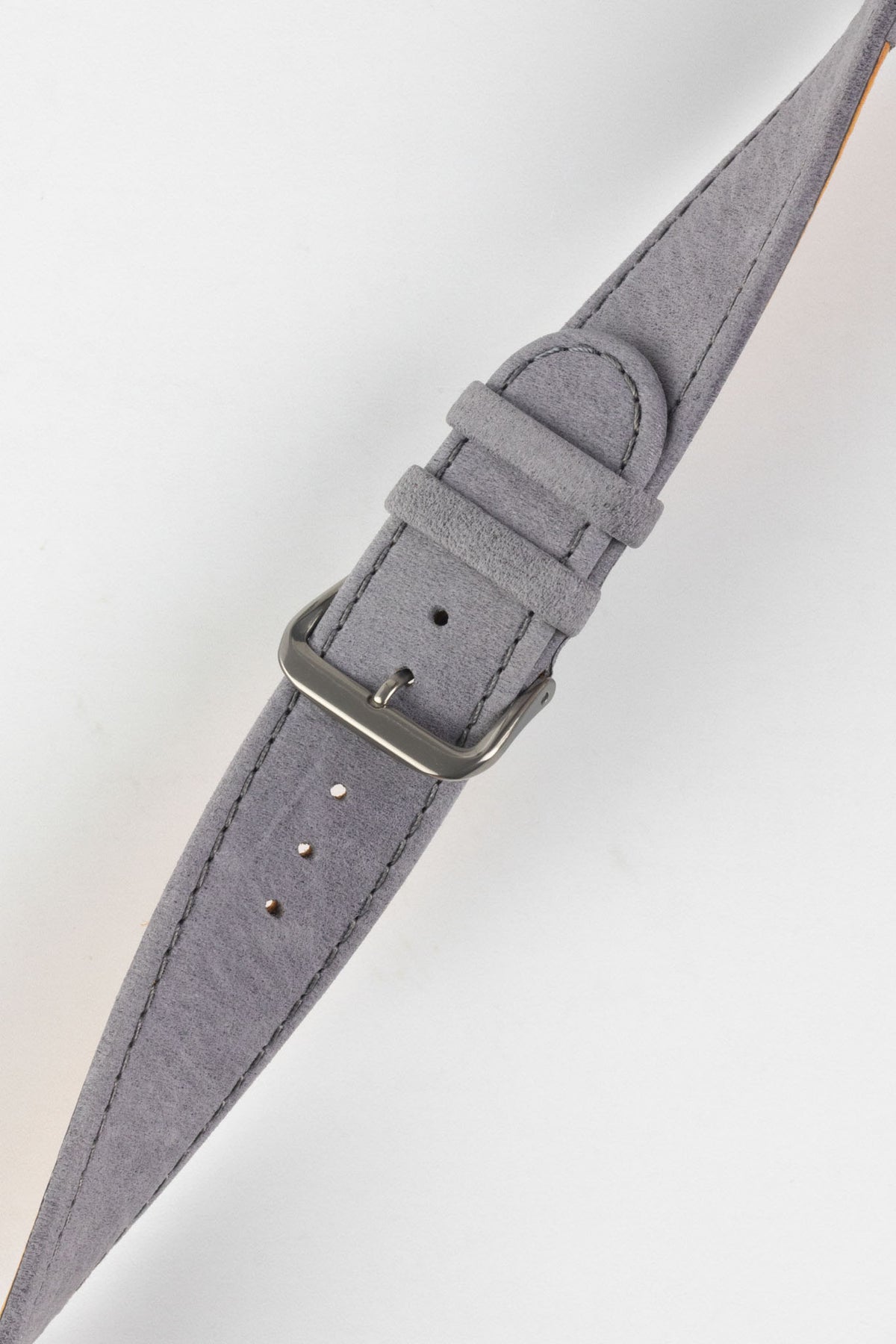 Close-up of a light grey nubuck leather watch strap with a soft matte finish, tonal grey stitching, dual keeper loops, multiple adjustment holes, and a brushed stainless steel buckle, displayed diagonally on a light grey background to highlight the tapered profile, supple suede-like texture, and premium handcrafted construction.