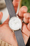 Close-up of a Tissot dress watch with a white multi-function dial and polished stainless steel case, fitted with a light grey nubuck leather watch strap featuring tonal stitching and a soft suede-like texture, held in hand to highlight the strap’s premium handcrafted construction, minimalist design, and refined contemporary styling.