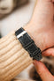 Close-up of a black leather watch strap worn on the wrist, featuring contrasting cream stitching, dual keeper loops, multiple adjustment holes, and a polished stainless steel buckle, shown with a cream knitted sweater cuff to highlight the strap's smooth matte finish, premium handcrafted construction, secure fit, and vintage-inspired design.