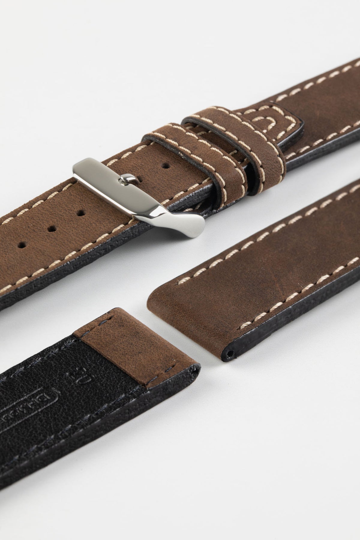 Close-up detail view of a dark brown leather watch strap displayed with one strap section detached, featuring a smooth vintage-style finish, cream contrast stitching, dual keeper loops, multiple adjustment holes, a polished stainless steel buckle, and a black leather lining embossed with the Di-Modell logo and size marking, shown on a light grey background to highlight the premium handcrafted construction, tapered profile, and quick-release spring bar compatibility.