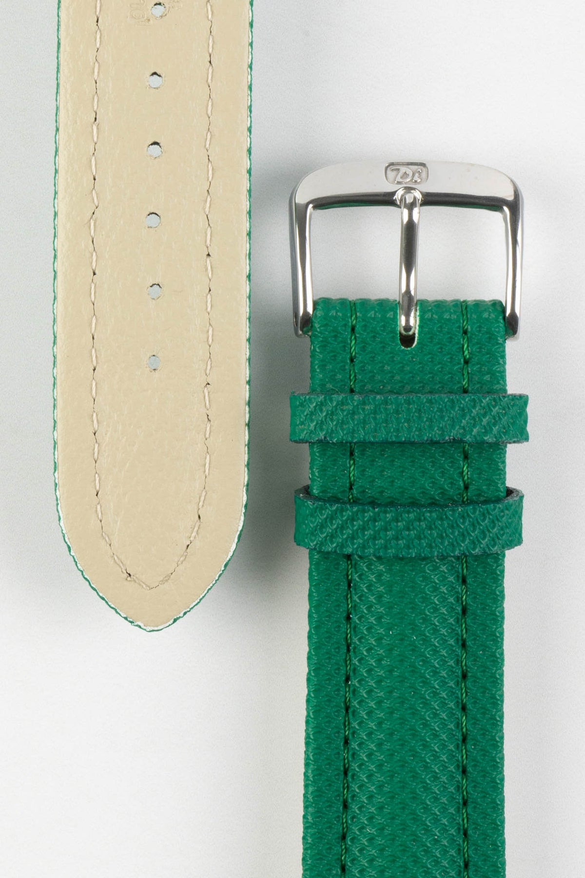 Close-up product photograph of a green textured leather watch strap displayed on a white background. The image shows both the top and underside of the strap, highlighting the fine embossed grain pattern, beige leather lining, matching green stitching, dual leather keepers, multiple sizing holes, and a polished stainless steel pin buckle engraved with the manufacturer's logo. The photograph showcases the strap's premium materials, craftsmanship, and classic tapered design.