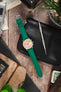 Studio Underd0g chronograph watch on a green textured leather strap, displayed with vintage accessories and watchmaking tools on a rustic wooden surface.