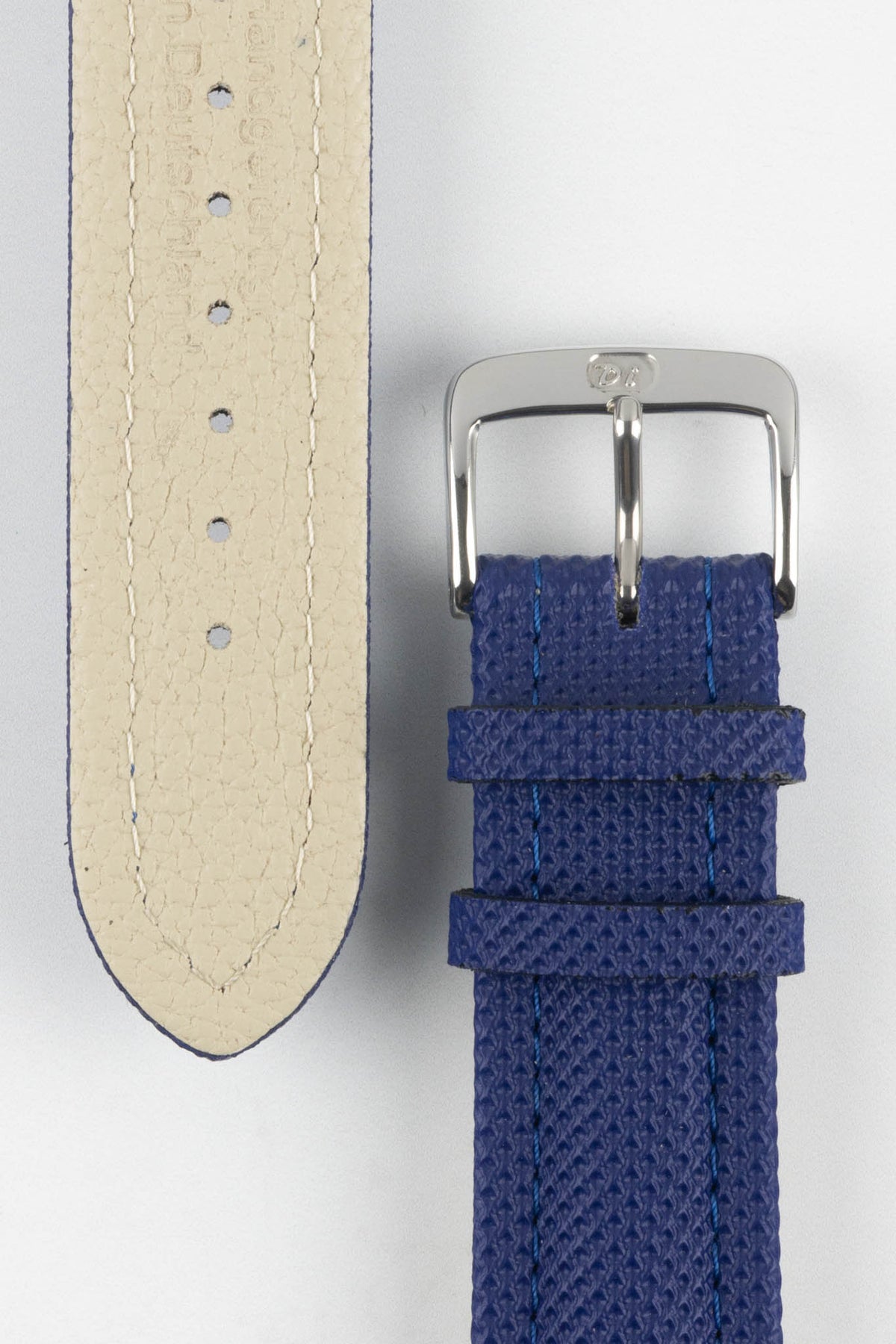 Close-up of a blue Di-Modell Traveller leather watch strap on a white background, showing the textured leather finish, polished stainless steel buckle, matching blue keepers, tonal blue stitching, beige leather-lined underside, multiple adjustment holes, and a rounded tip.