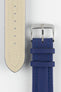 Close-up of a blue Di-Modell Traveller leather watch strap on a white background, showing the textured leather finish, polished stainless steel buckle, matching blue keepers, tonal blue stitching, beige leather-lined underside, multiple adjustment holes, and a rounded tip.