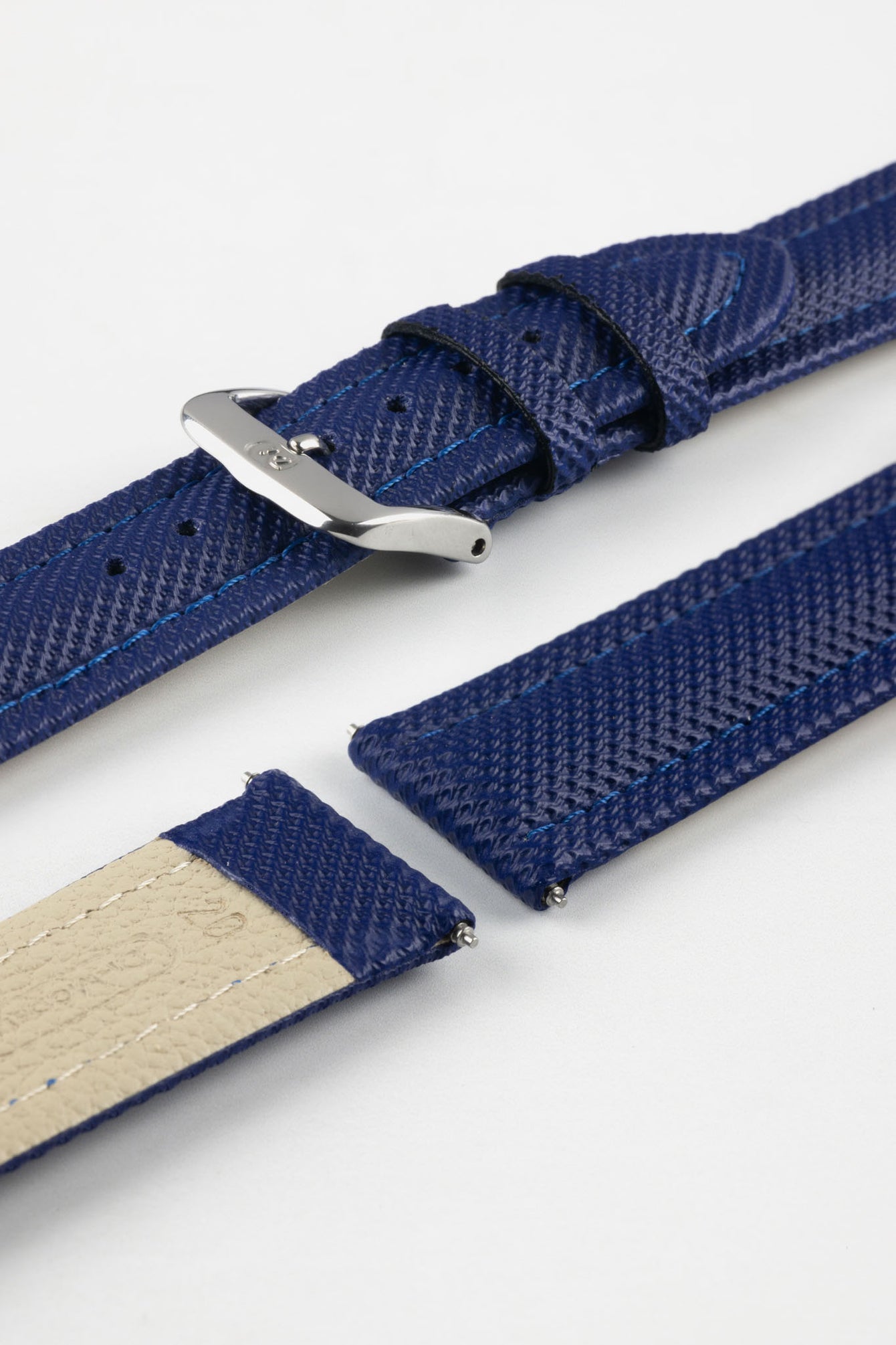 Close-up of a blue Di-Modell Traveller leather watch strap shown in separate pieces on a white background. Features a textured leather finish, polished stainless steel buckle, matching blue keepers, tonal blue stitching, quick-release spring bars, and a beige leather-lined underside.