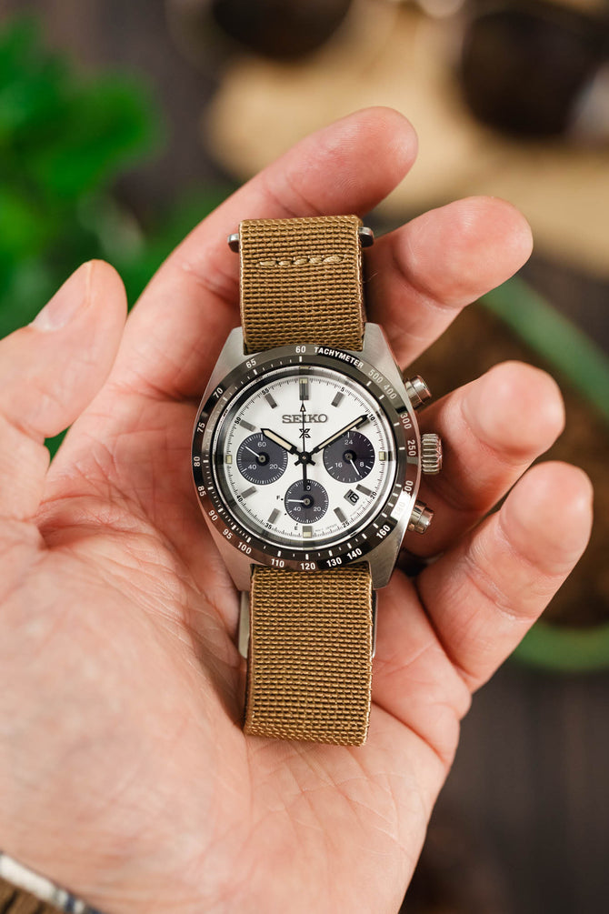 Panda dial watch on a in a hand fitted to a brown parachute webbing watch strap with brushed stainless steel hardware