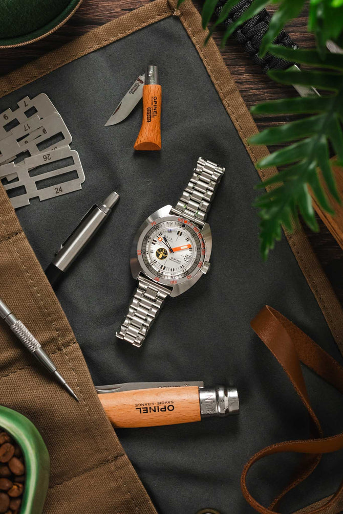 Lay flat photograph of Doxa Sub 300 Searambler Watch lay on open watch roll with tools and knives on a Forstner Stainless steel bracelet