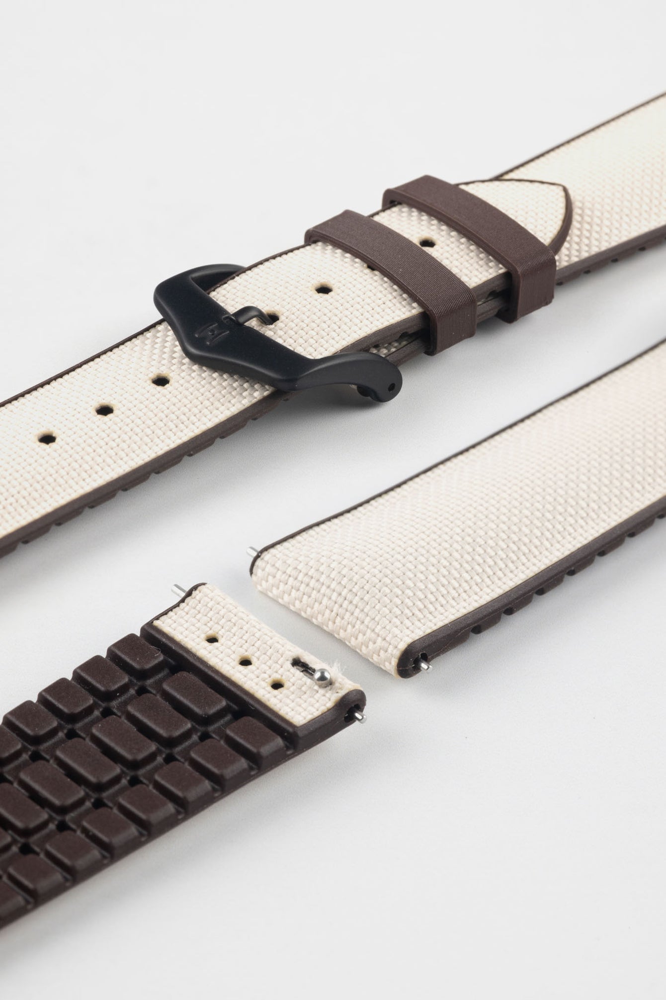 Beige textile-effect watch strap with brown rubber backing and a black buckle, shown in separate sections on a white background. Features a woven-look surface, brown edges, and a patterned rubber underside.
