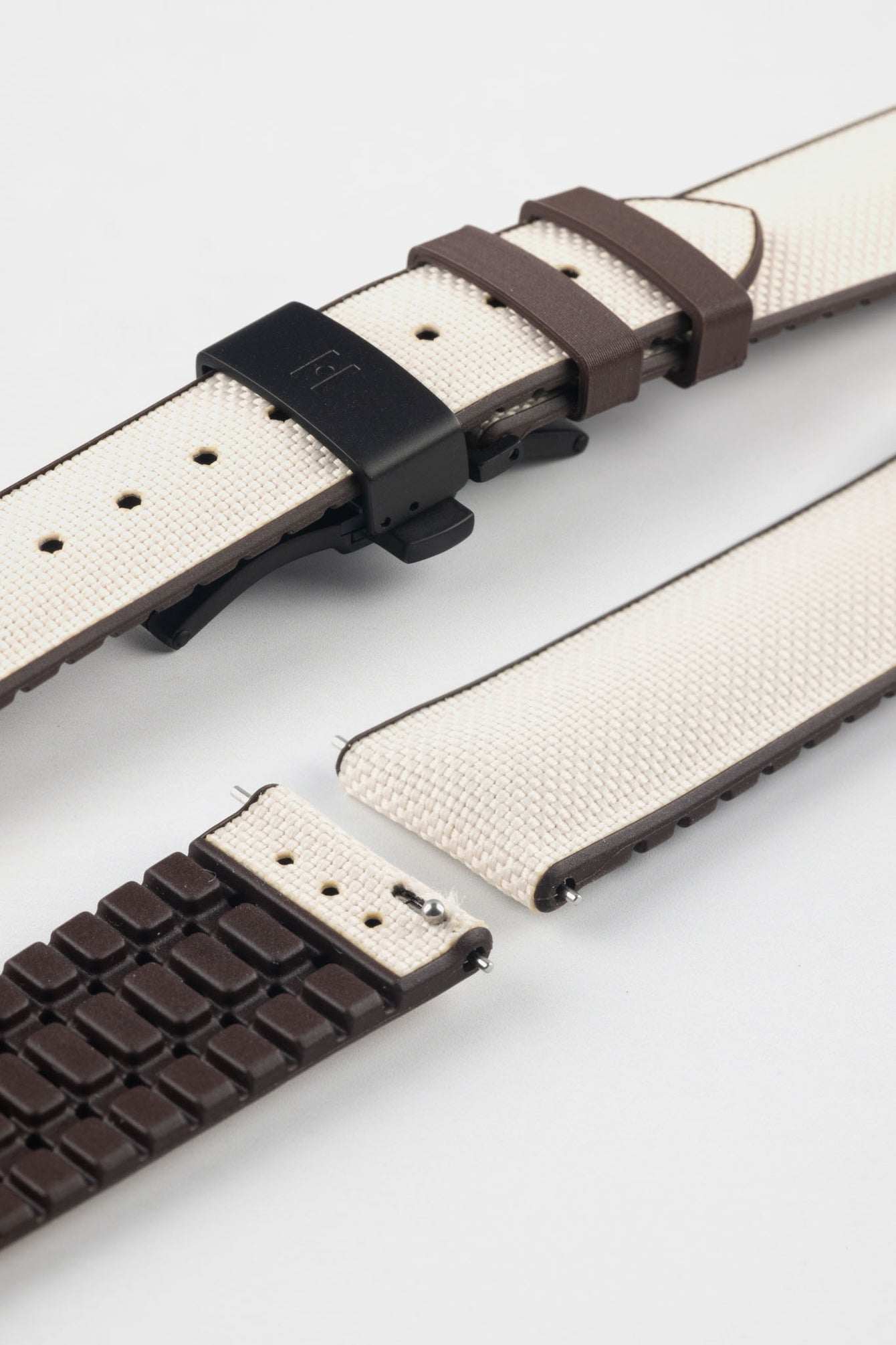 Beige textile-effect watch strap with brown rubber backing and a black deployment clasp, shown in separate sections on a white background. Features a woven-look surface, brown edges, and a patterned rubber underside.