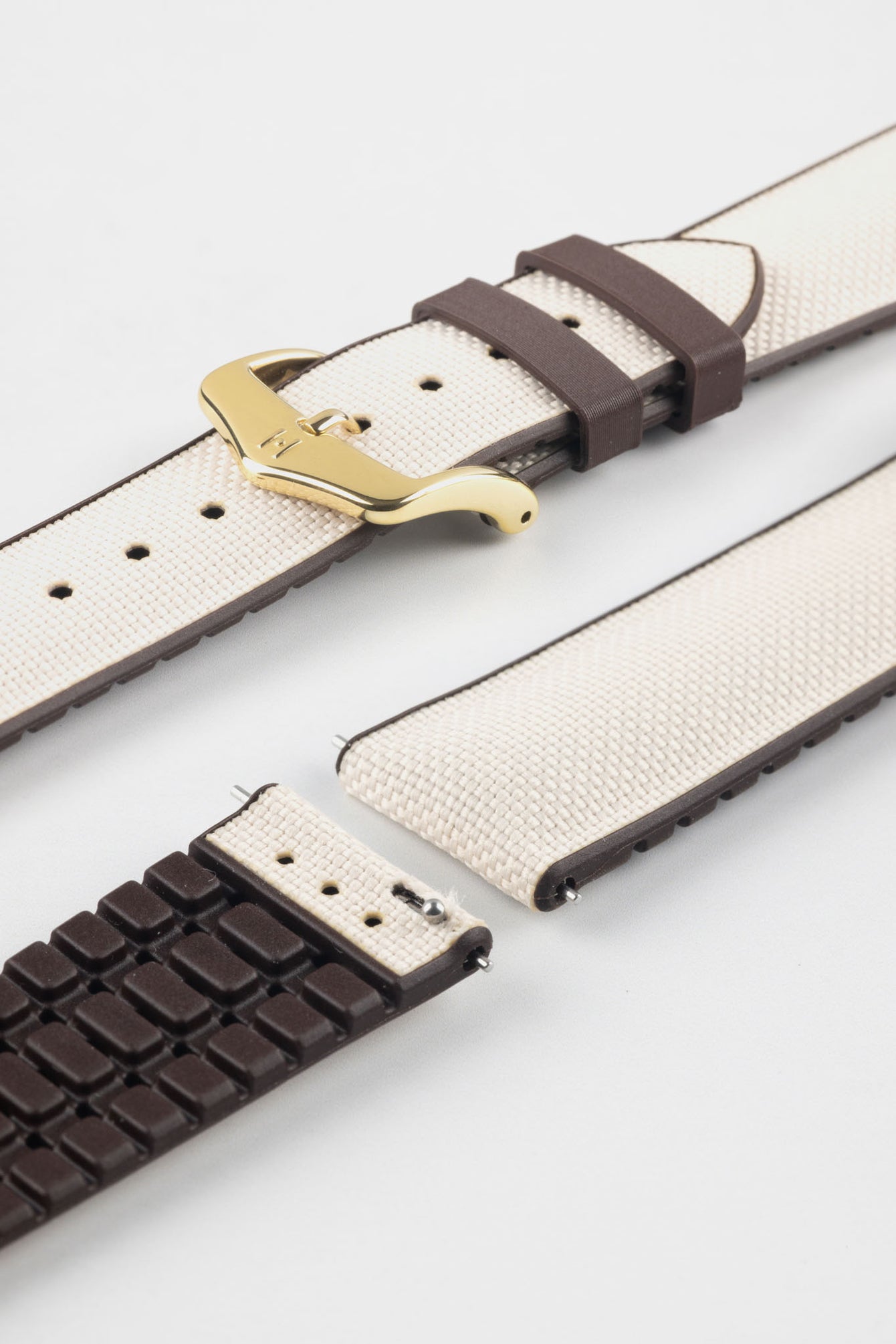Beige textile-effect watch strap with brown rubber backing and a gold-tone buckle, shown in separate sections on a white background. Features a woven-look surface, brown edges, and a patterned rubber underside.