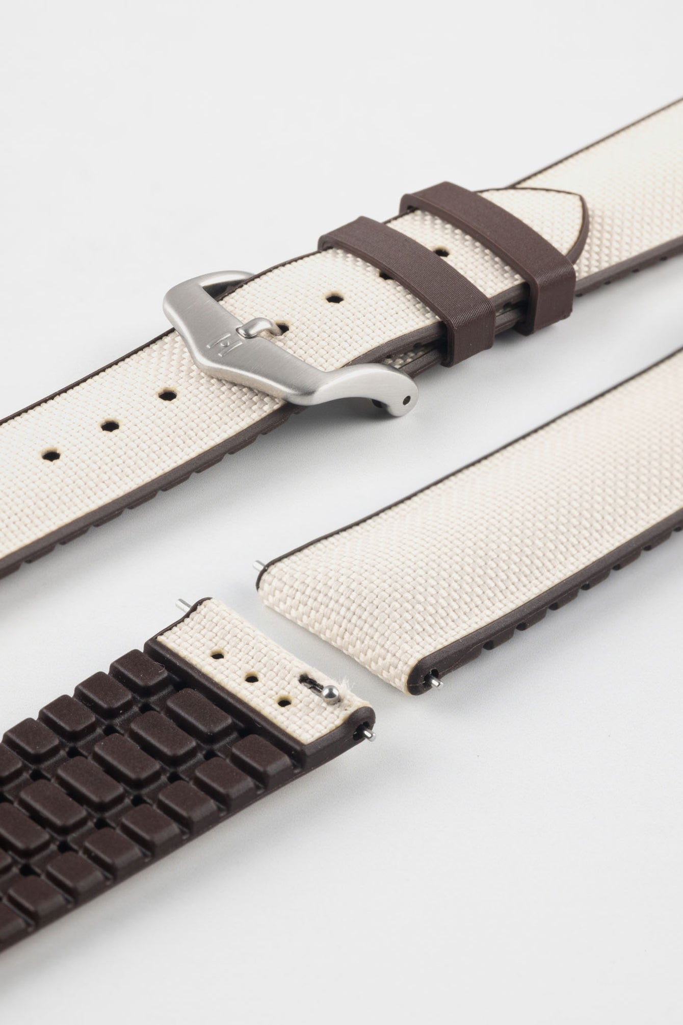 Beige textile-effect watch strap with brown rubber backing and a brushed silver-tone buckle, shown in separate sections on a white background. Features a woven-look surface, brown edges, and a patterned rubber underside.