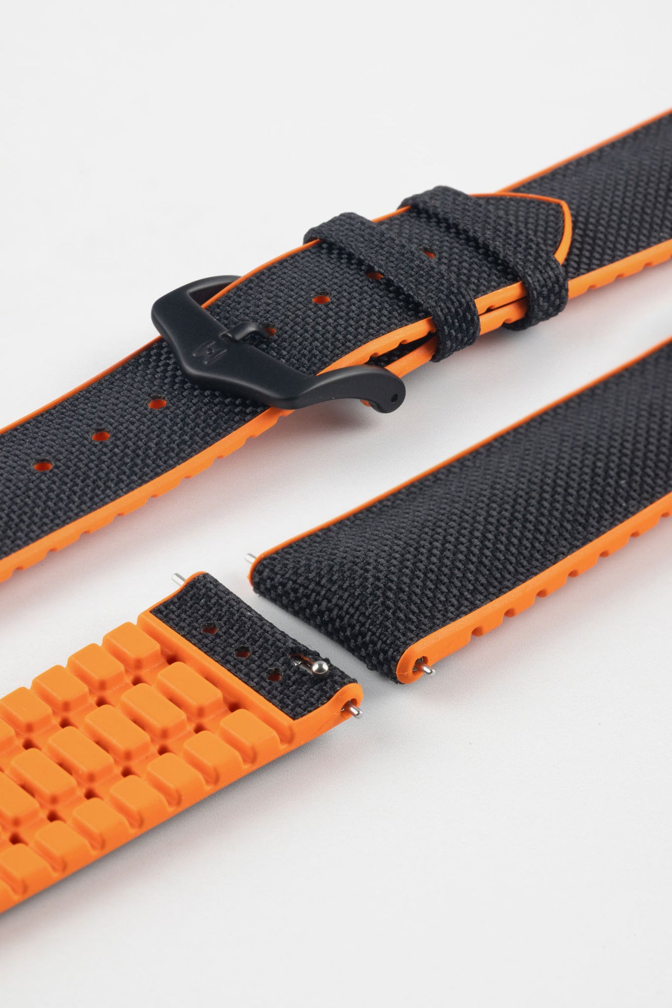 Black textile-effect watch strap with bright orange rubber backing and a black buckle, shown in separate sections on a white background. Features a textured woven-look surface, orange edges, and a patterned rubber underside.