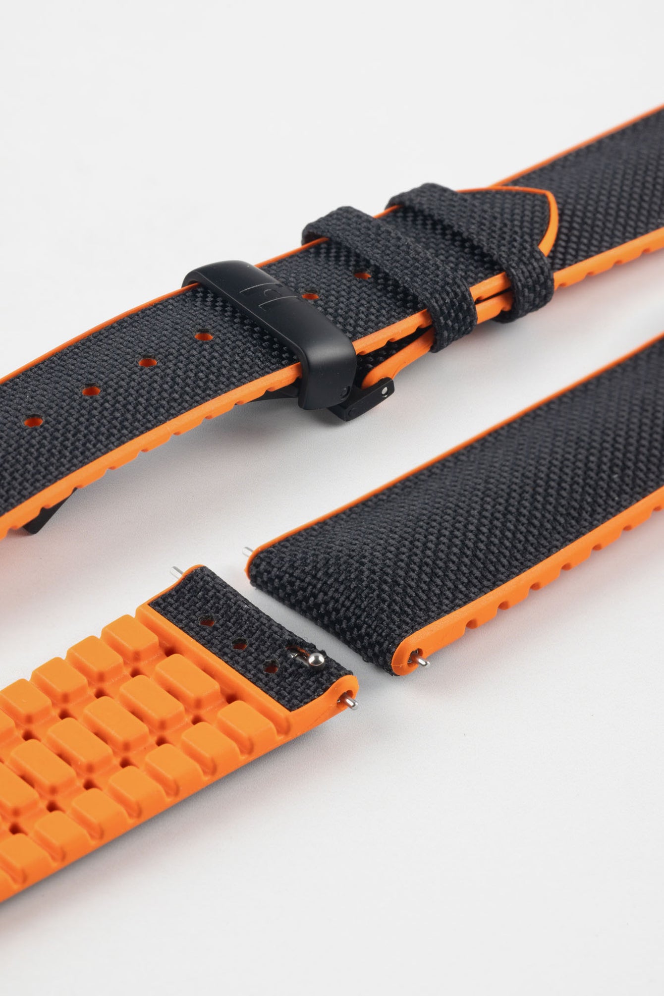 Black textile-effect watch strap with bright orange rubber backing and a black deployment clasp, shown in separate sections on a white background. Features a textured woven-look surface, orange edges, and a patterned rubber underside.