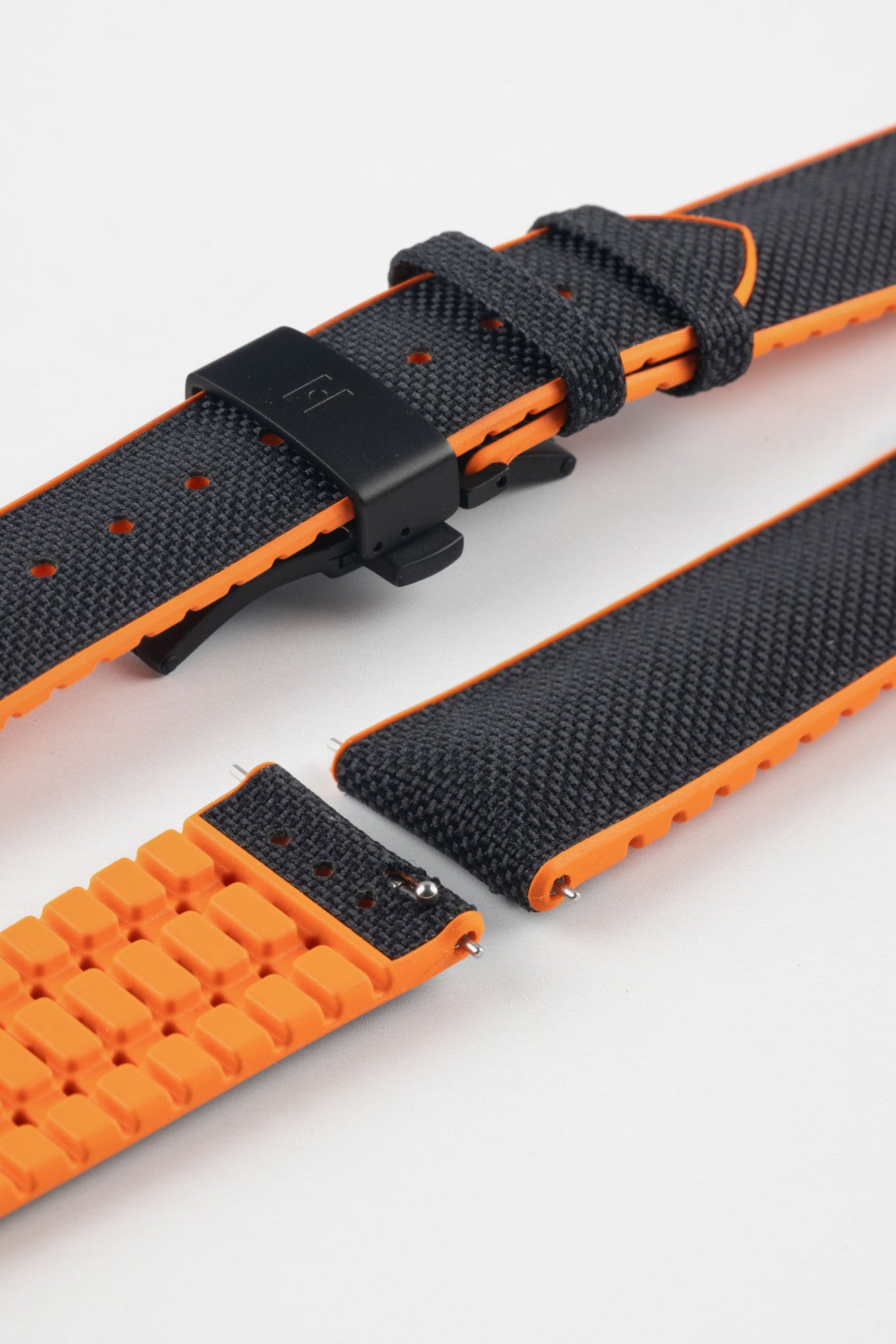 Black textile-effect watch strap with bright orange rubber backing and a black deployment clasp, shown in separate sections on a white background. Features a textured woven-look surface, orange edges, and a patterned rubber underside.