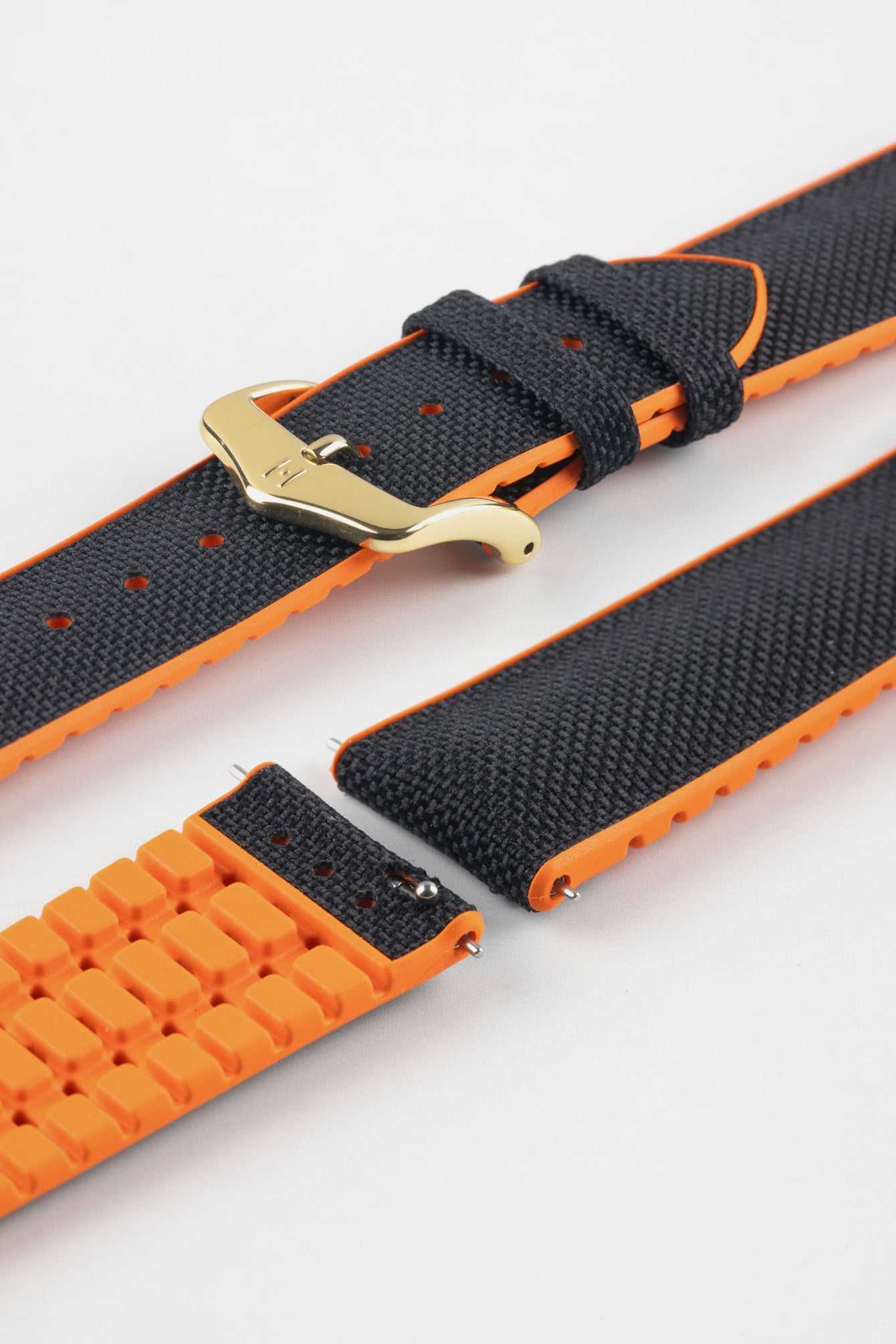 Black textile-effect watch strap with bright orange rubber backing and a gold-tone buckle, shown in separate sections on a white background. Features a textured woven-look surface, orange edges, and a patterned rubber underside.