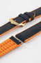 Black textile-effect watch strap with bright orange rubber backing and a gold-tone buckle, shown in separate sections on a white background. Features a textured woven-look surface, orange edges, and a patterned rubber underside.