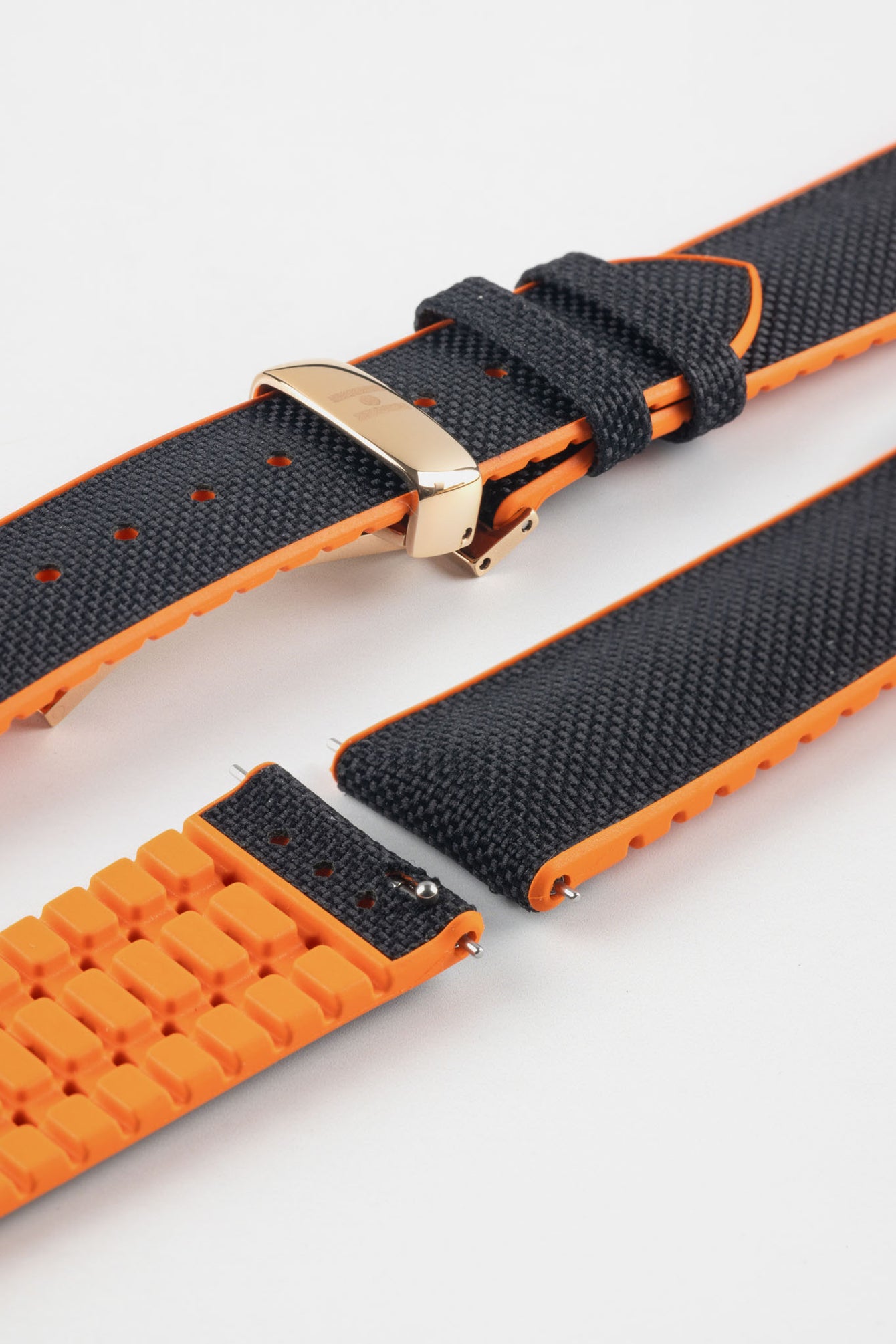 Black textile-effect watch strap with bright orange rubber backing and a rose gold-tone deployment clasp, shown in separate sections on a white background. Features a woven-look texture, orange edges, and a patterned rubber underside.