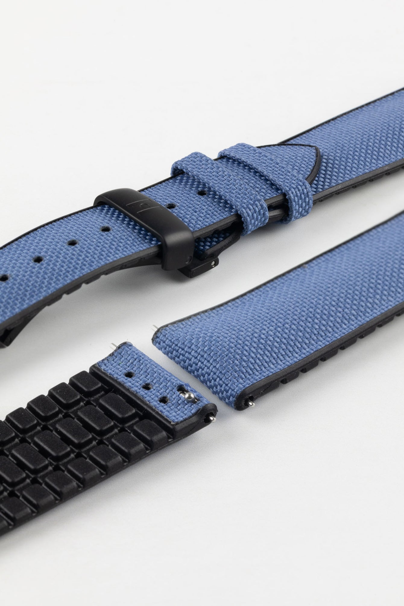 A detailed, slightly angled shot of a blue Hirsch Arne Performance Watch Strap, laid in two pieces on a white background, highlighting its woven blue upper, black ribbed underside, and a black deployment clasp.