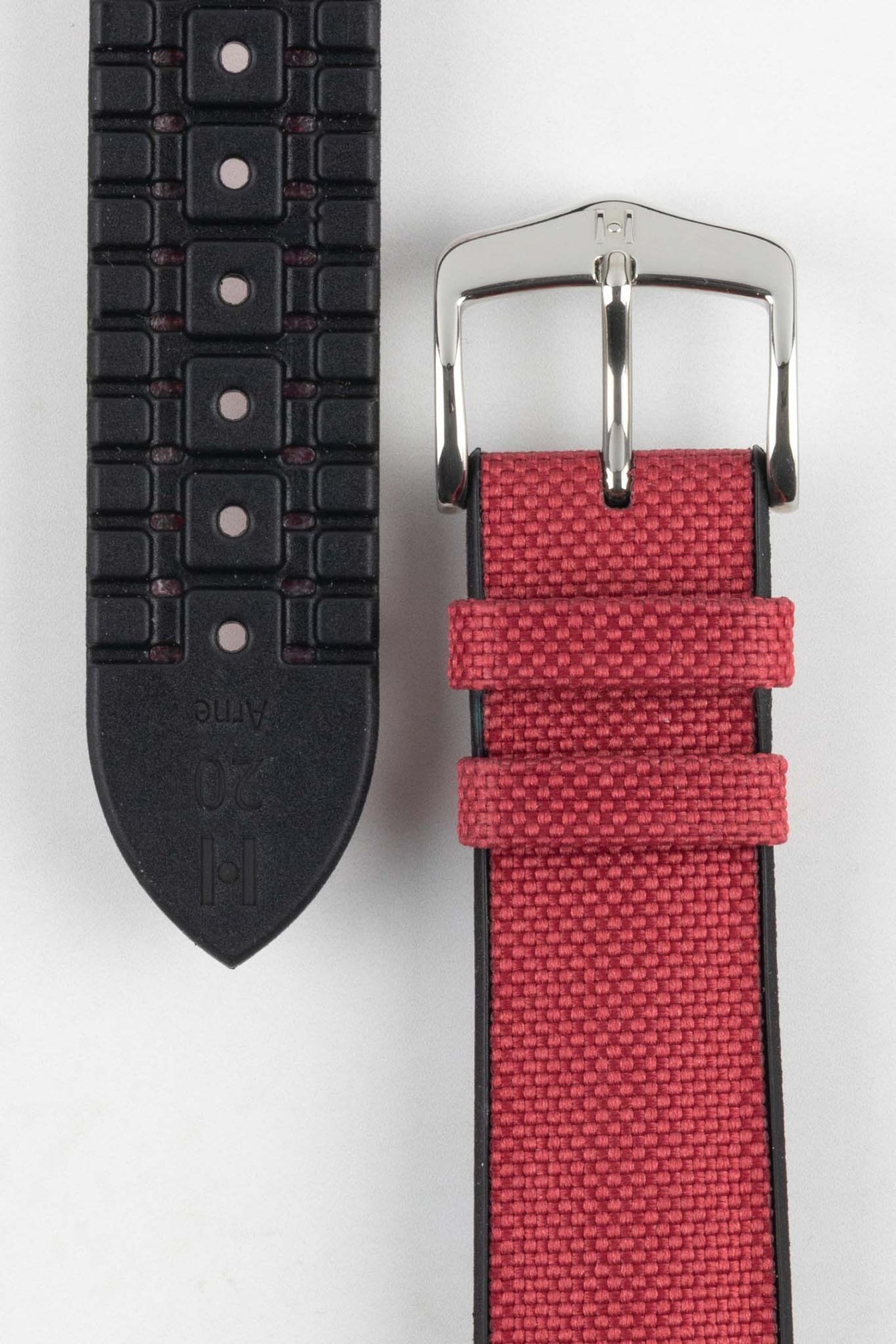 A detailed close-up of a burgundy Hirsch Arne Performance watch strap laid out on a white surface. The image clearly shows the textured red fabric on the top, the black rubberized underside with ventilation channels and the word "Arne" and "20" embossed, and the polished silver buckle.