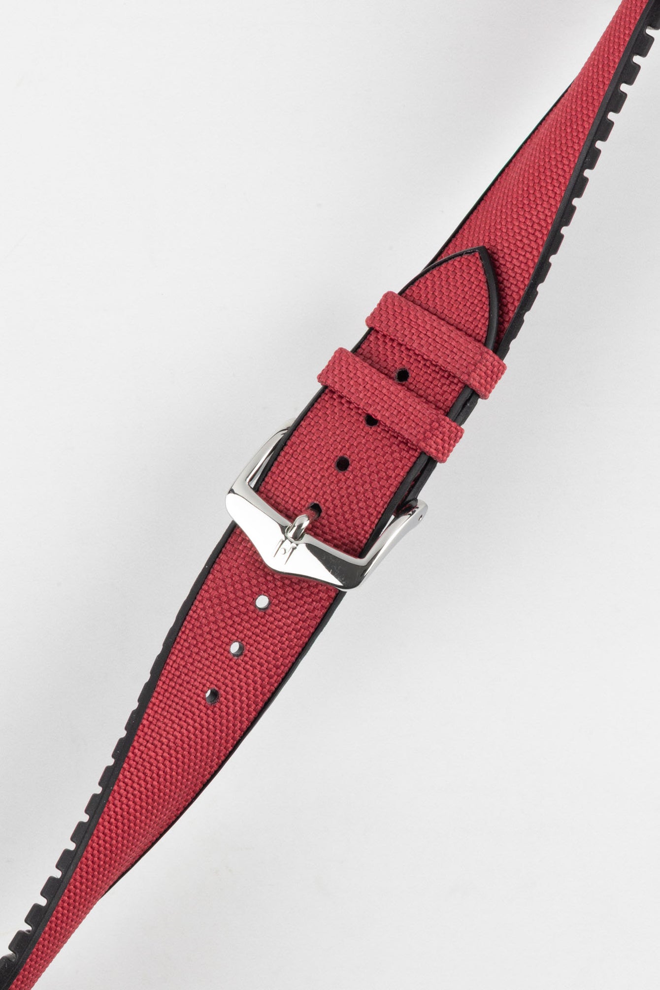 A diagonal close-up of a burgundy Hirsch Arne Performance watch strap with a polished silver buckle, set against a bright white background. The textured surface of the red strap and the black lining are clearly visible.