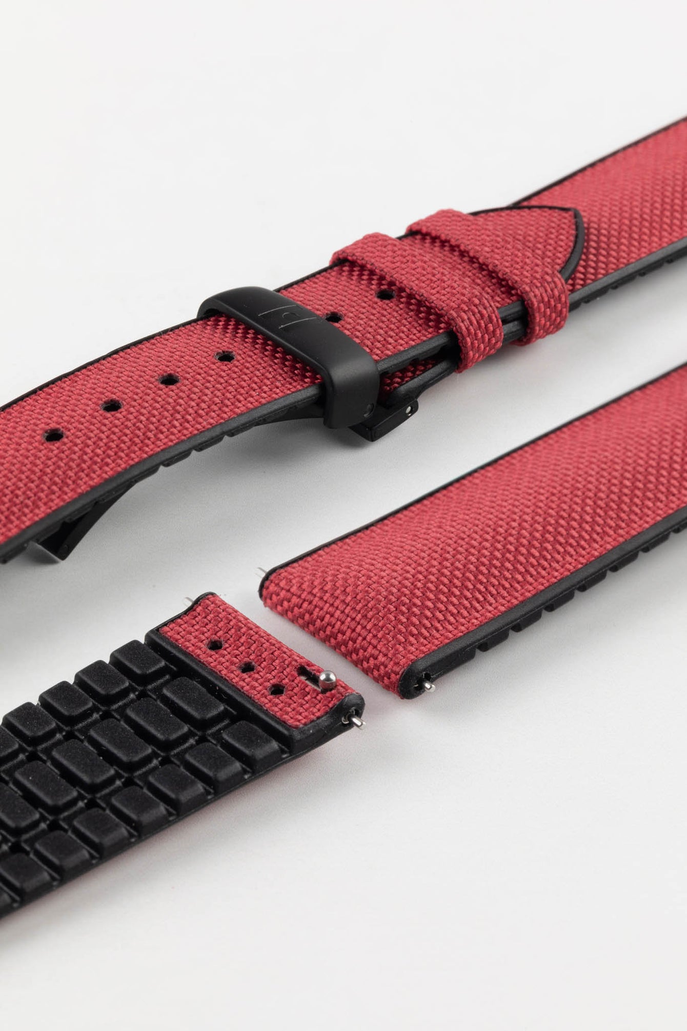 A burgundy Hirsch Arne Animal-Free Sailcloth Effect Performance Watch Strap is displayed on a white background, showcasing the strap's full length and a matte black sport deployment clasp. The textured sailcloth-like material of the strap is also clearly visible, along with the black rubberized underside.