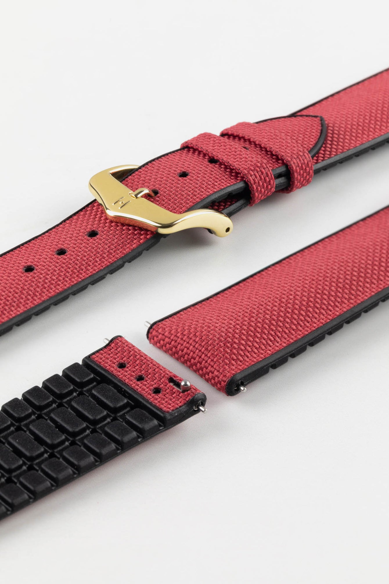 A burgundy Hirsch Arne Animal-Free Sailcloth Effect Performance Watch Strap is displayed on a white background, showcasing the strap's full length and a gold pin buckle. The textured sailcloth-like material of the strap is also clearly visible, along with the black rubberized underside.