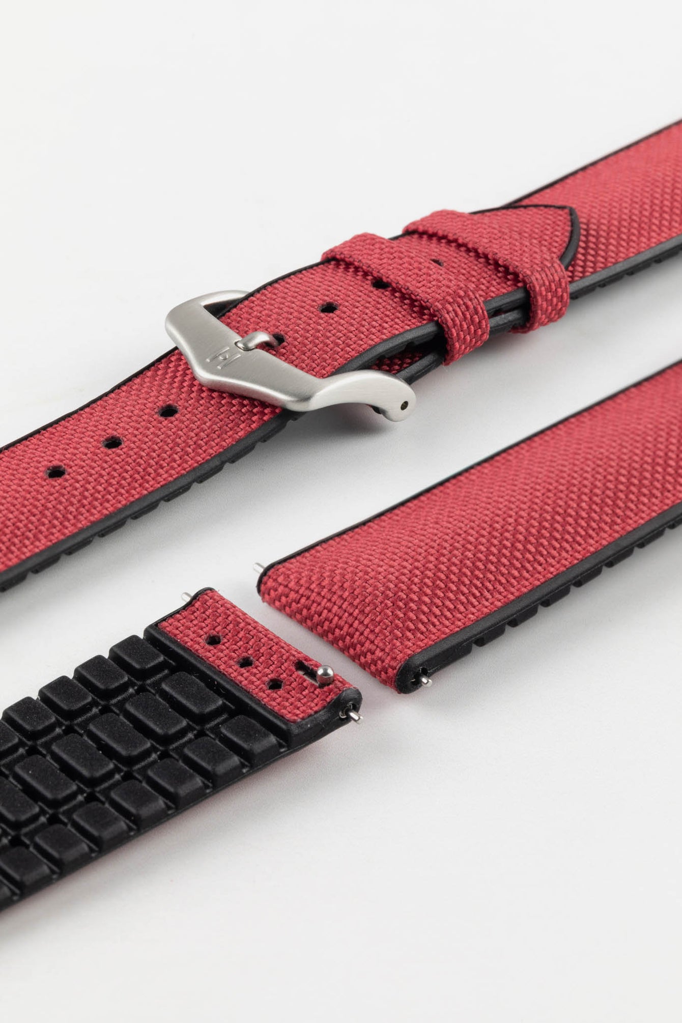 A burgundy Hirsch Arne Animal-Free Sailcloth Effect Performance Watch Strap is displayed on a white background, showcasing the strap's full length and a brushed steel pin buckle. The textured sailcloth-like material of the strap is also clearly visible, along with the black rubberized underside.