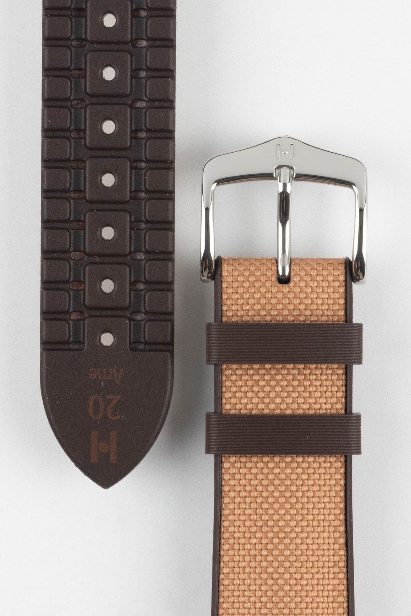 Golden brown textile-effect watch strap shown from the front and underside on a white background. Features a silver-tone buckle, brown edges, woven-look texture, and a patterned brown rubber backing with multiple adjustment holes.