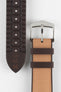 Golden brown textile-effect watch strap shown from the front and underside on a white background. Features a silver-tone buckle, brown edges, woven-look texture, and a patterned brown rubber backing with multiple adjustment holes.