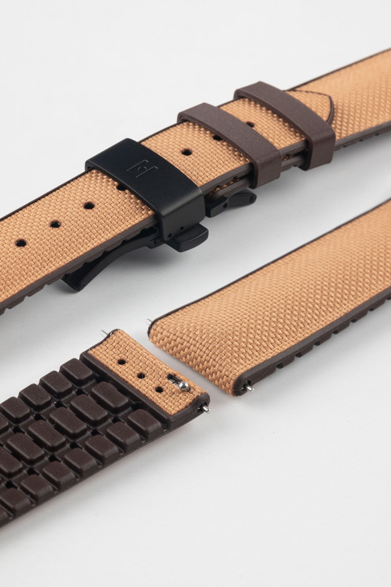 Golden brown textile-effect watch strap with brown rubber backing and a black deployment clasp, shown in separate sections on a white background. Features a woven-look surface, brown edges, and a patterned rubber underside.