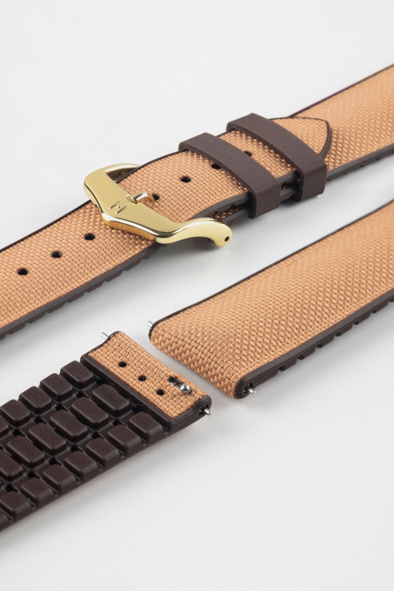Golden brown textile-effect watch strap with brown rubber backing and a gold-tone buckle, shown in separate sections on a white background. Features a woven-look surface, brown edges, and a patterned rubber underside.