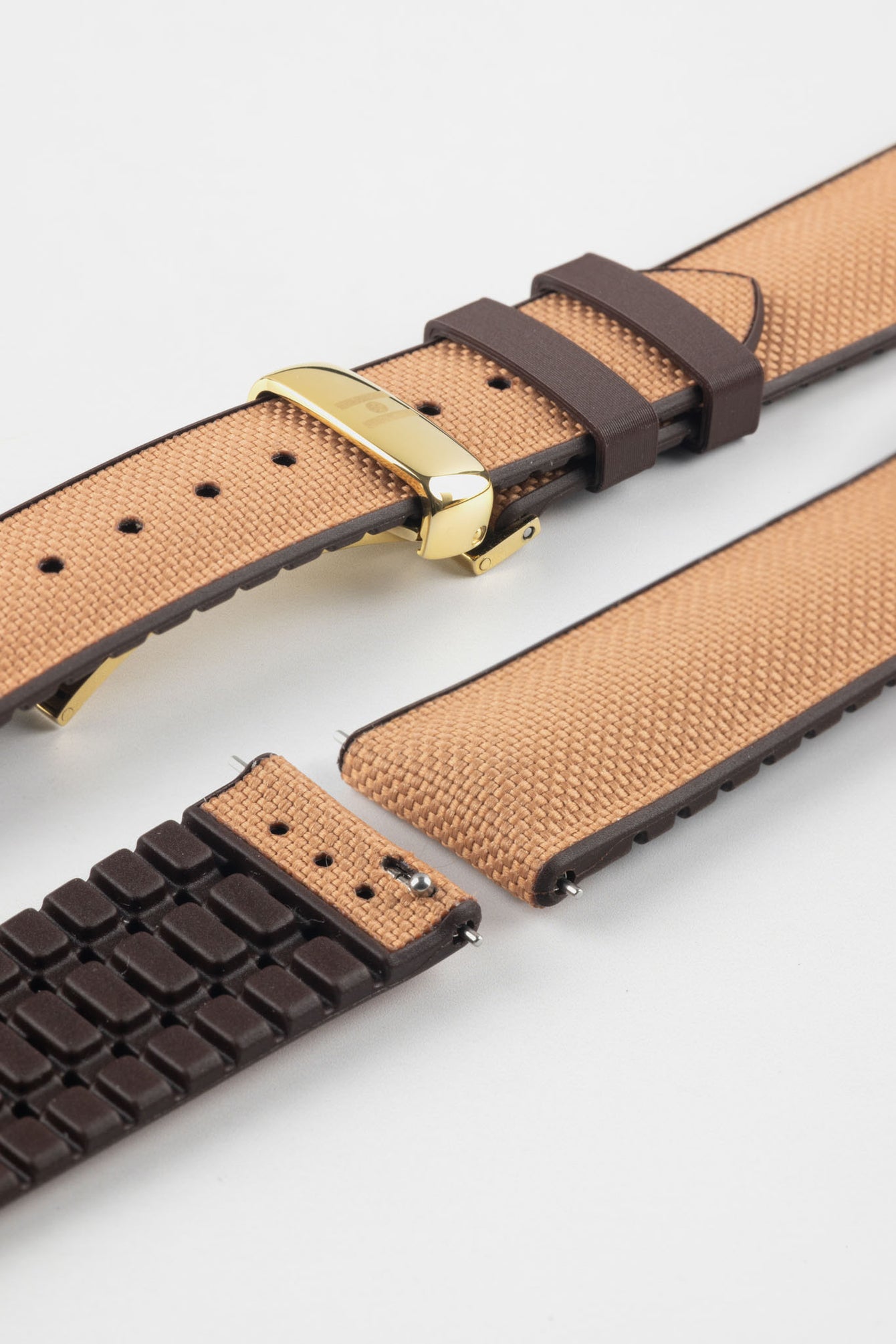 Golden brown textile-effect watch strap with brown rubber backing and a gold-tone deployment clasp, shown in separate sections on a white background. Features a woven-look surface, brown edges, and a patterned rubber underside.