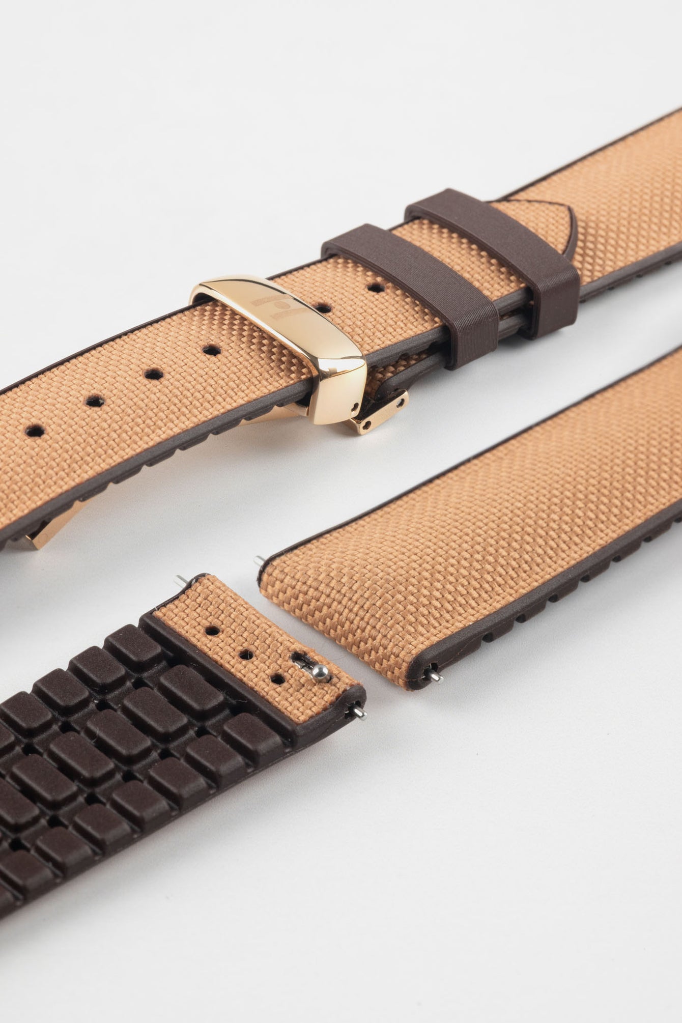 Golden brown textile-effect watch strap with brown rubber backing and a rose gold-tone deployment clasp, shown in separate sections on a white background. Features a woven-look surface, brown edges, and a patterned rubber underside.